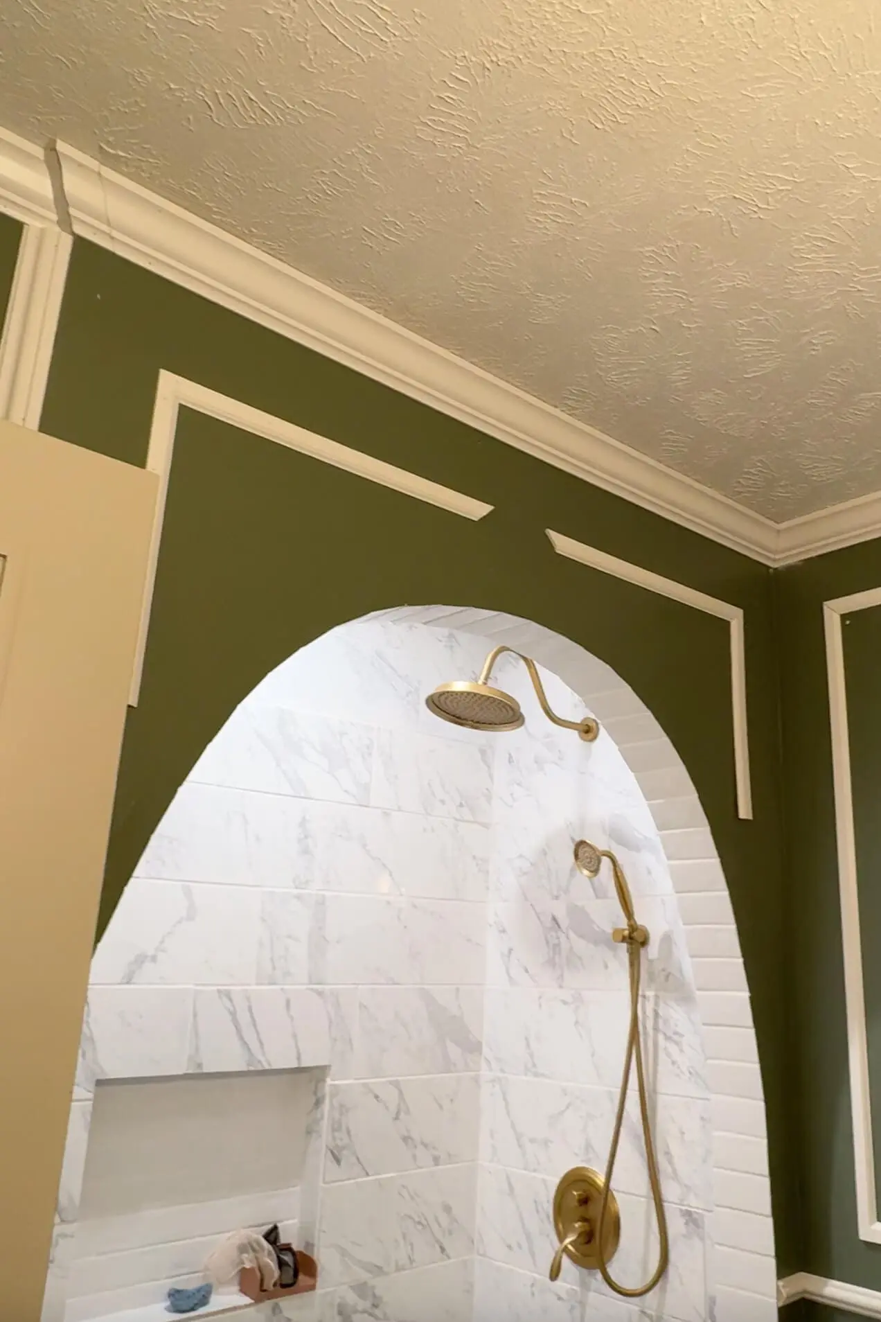 Completed bathroom renovation showcasing an arched shower entrance framed by decorative white trim. The green wall is accented by crisp, white molding, complementing the marble-tiled shower area with a sleek gold showerhead and handheld fixture.